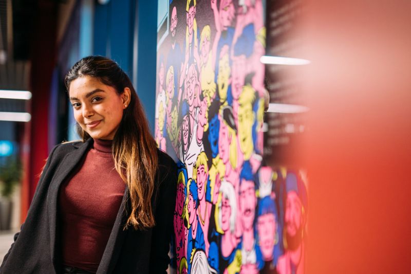 female student standing against a colourful wall smiling to camera